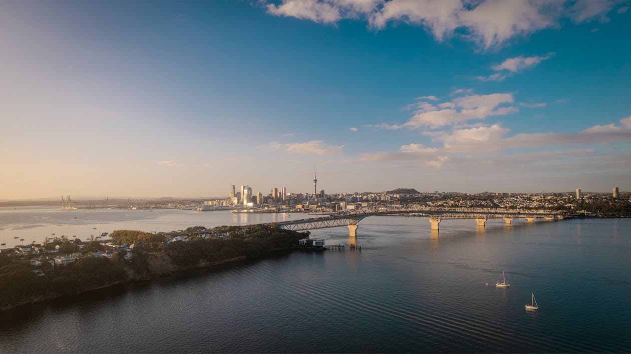 Auckland skyline and Harbour Bridge viewed across the water at sunrise, representing New Zealand relocation, migration, and settling into life in Auckland.