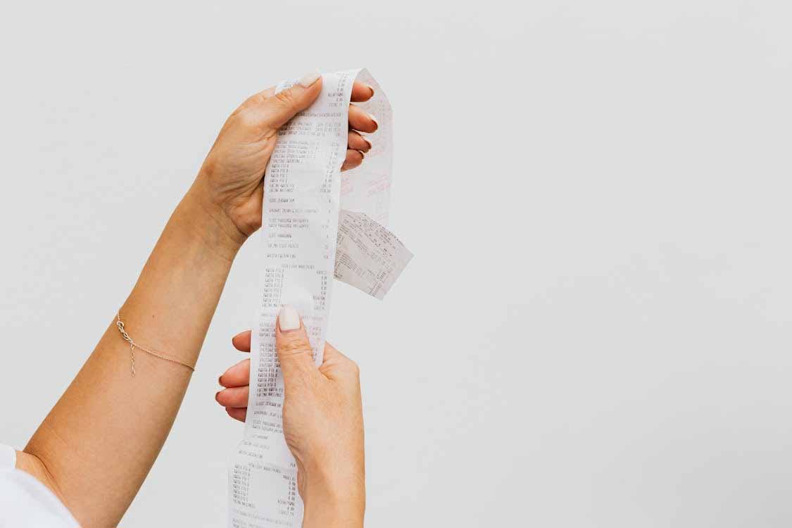 Person holding a long shopping receipt, representing household expenses, budgeting, and reviewing spending to free up money for a mortgage.