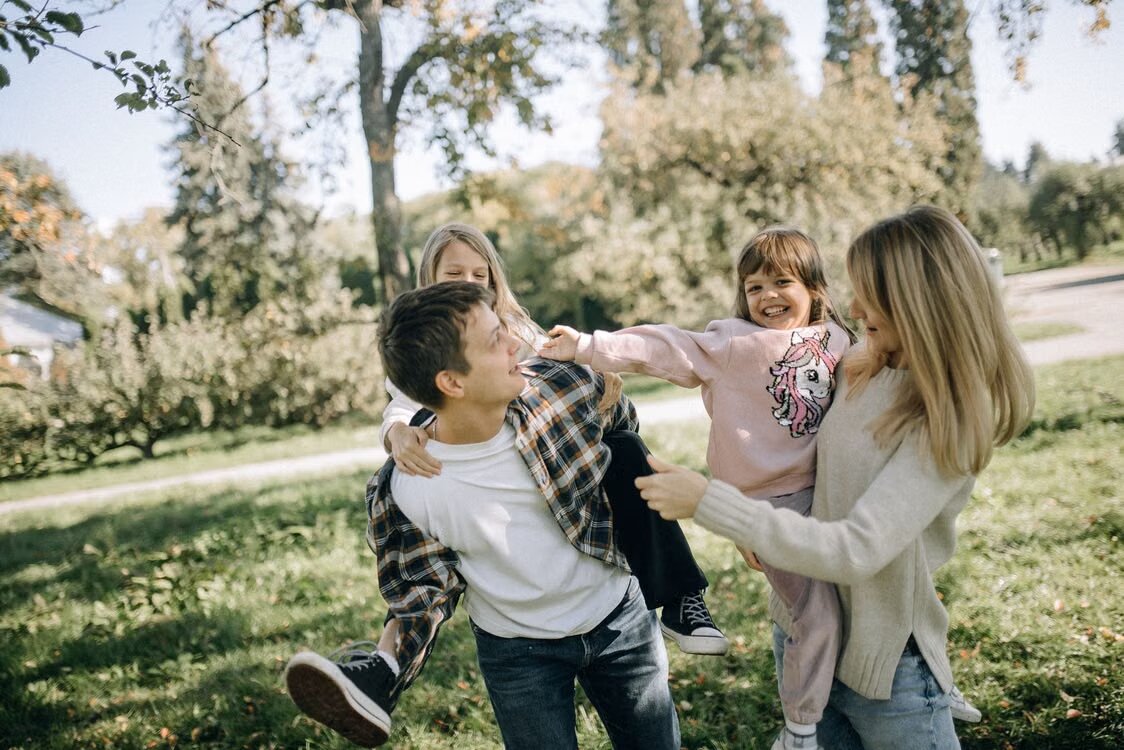 Parents playing with their two young daughters in an autumn park, representing family help with buying a first home