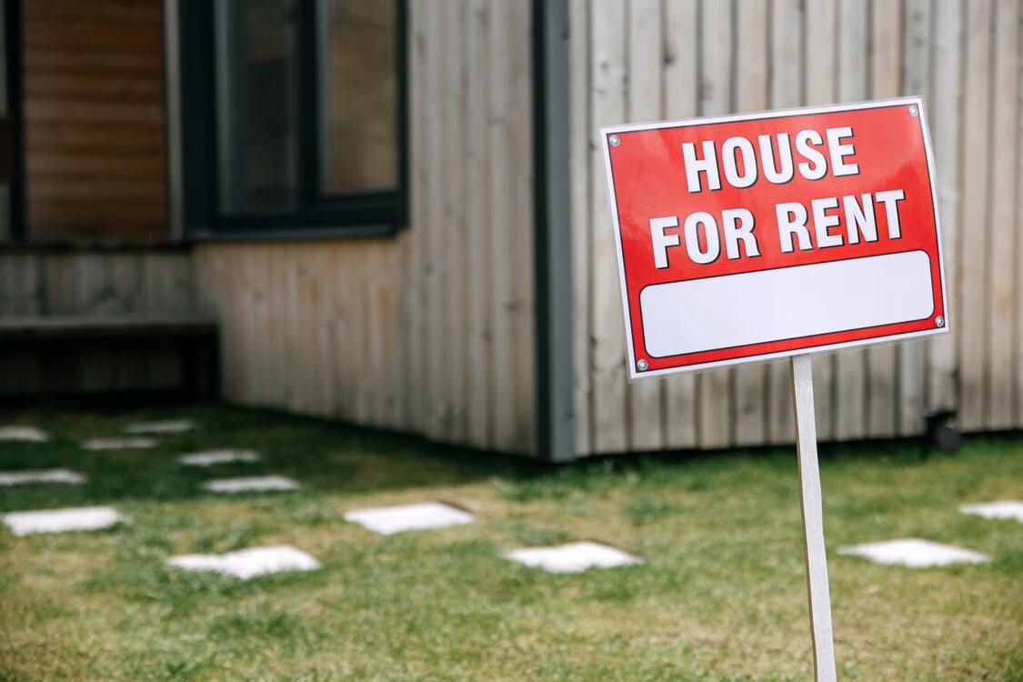 House for rent sign on the front lawn of a timber-clad home, representing keeping your current home as a rental